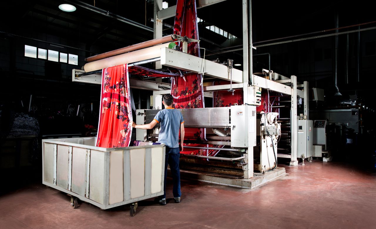 Home Worker operates machinery in a textile factory, overseeing fabric production.